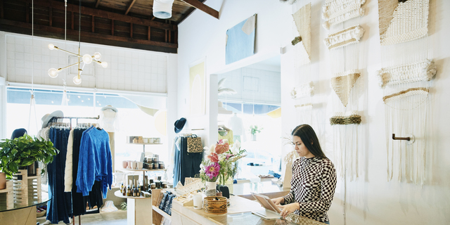 Shop owner working on digital tablet behind counter in clothing boutique