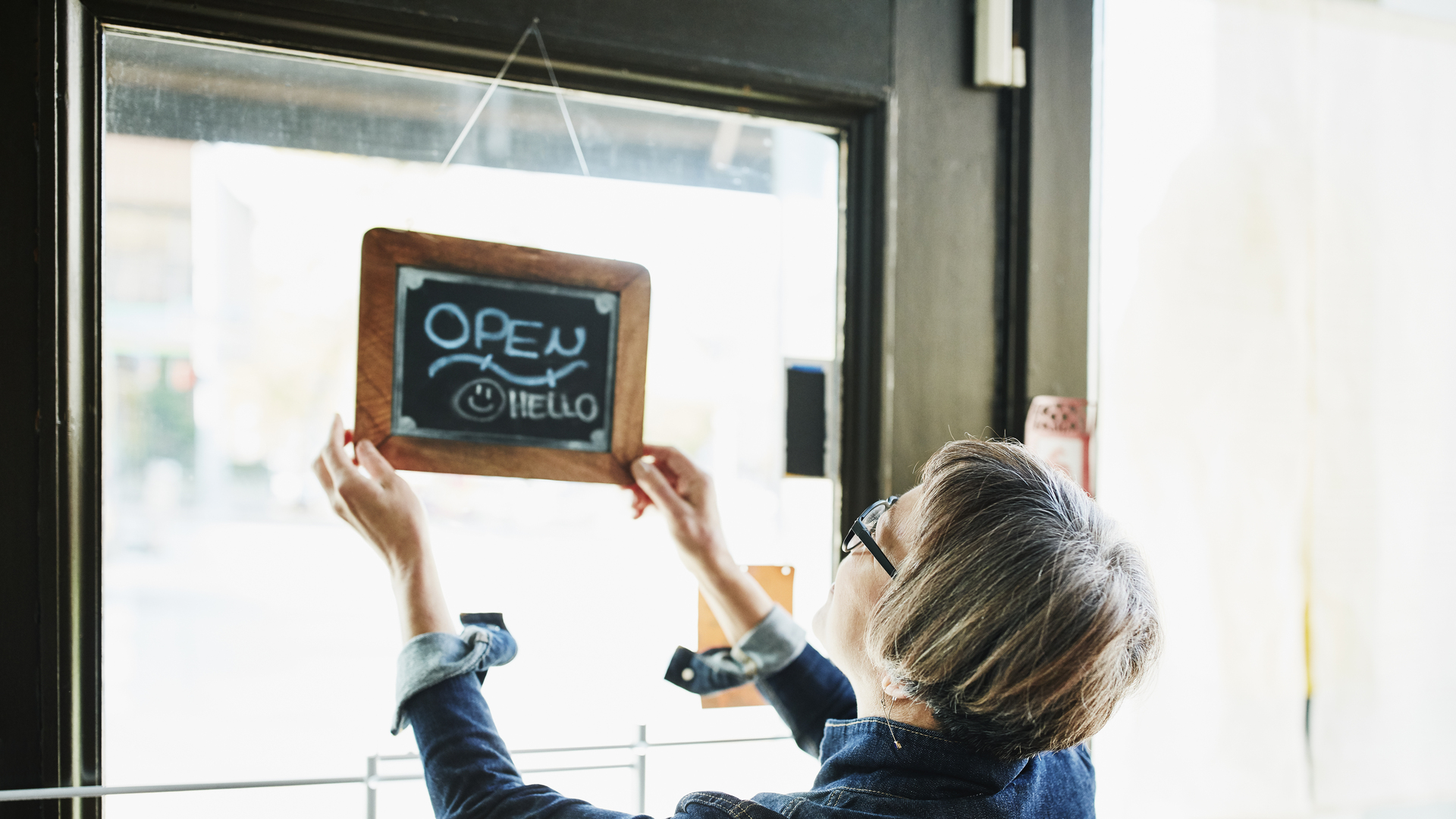 Senior female business owner turning open sign on door before opening boutique