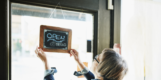 Senior female business owner turning open sign on door before opening boutique