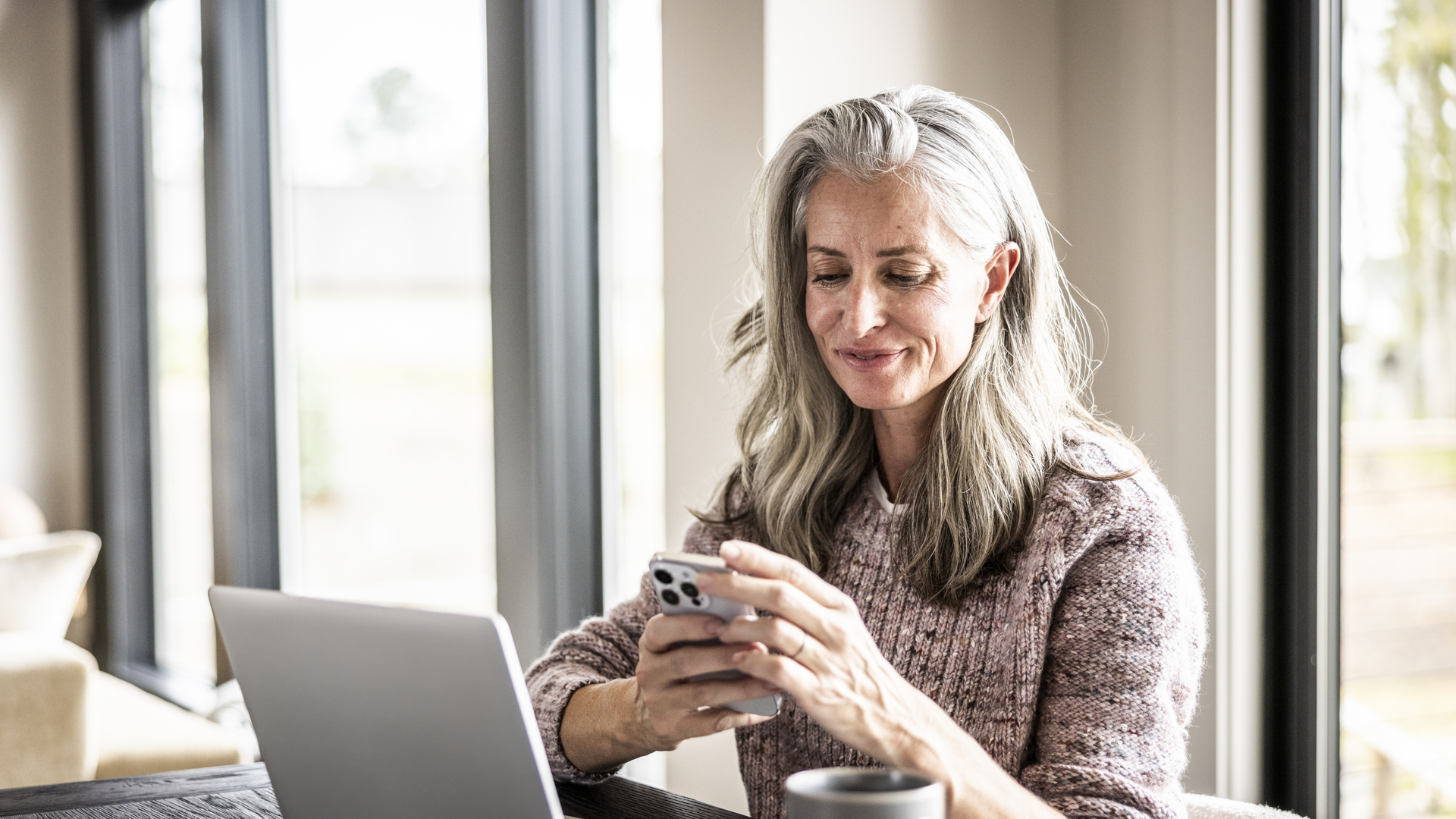 Senior woman using smartphone and laptop at home