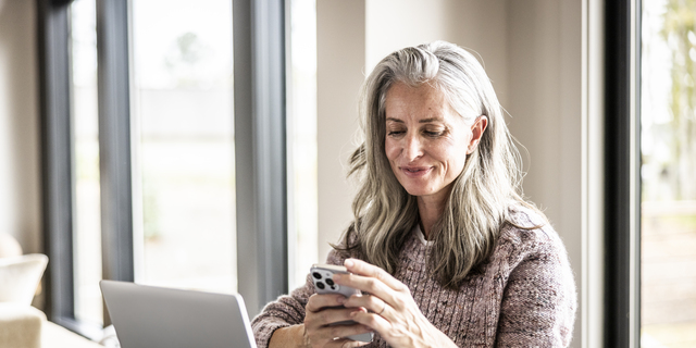 Senior woman using smartphone and laptop at home