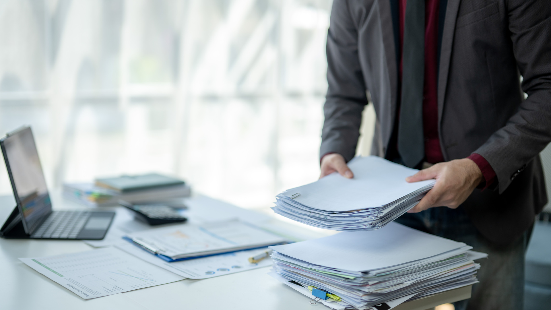 A man is sitting at a desk with a pile of papers in front of him
