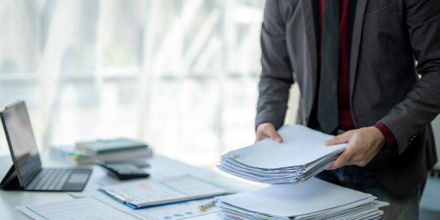 A man is sitting at a desk with a pile of papers in front of him