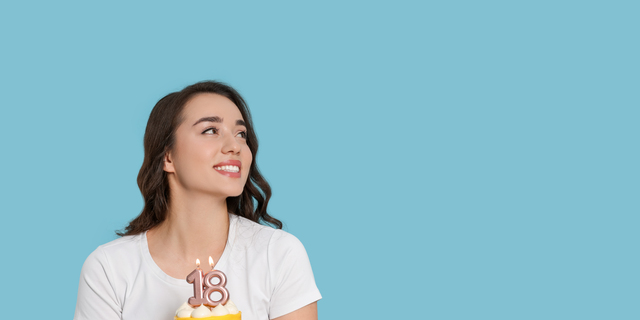 Coming of age party - 18th birthday. Woman holding delicious cake with number shaped candles on light blue background, space for text