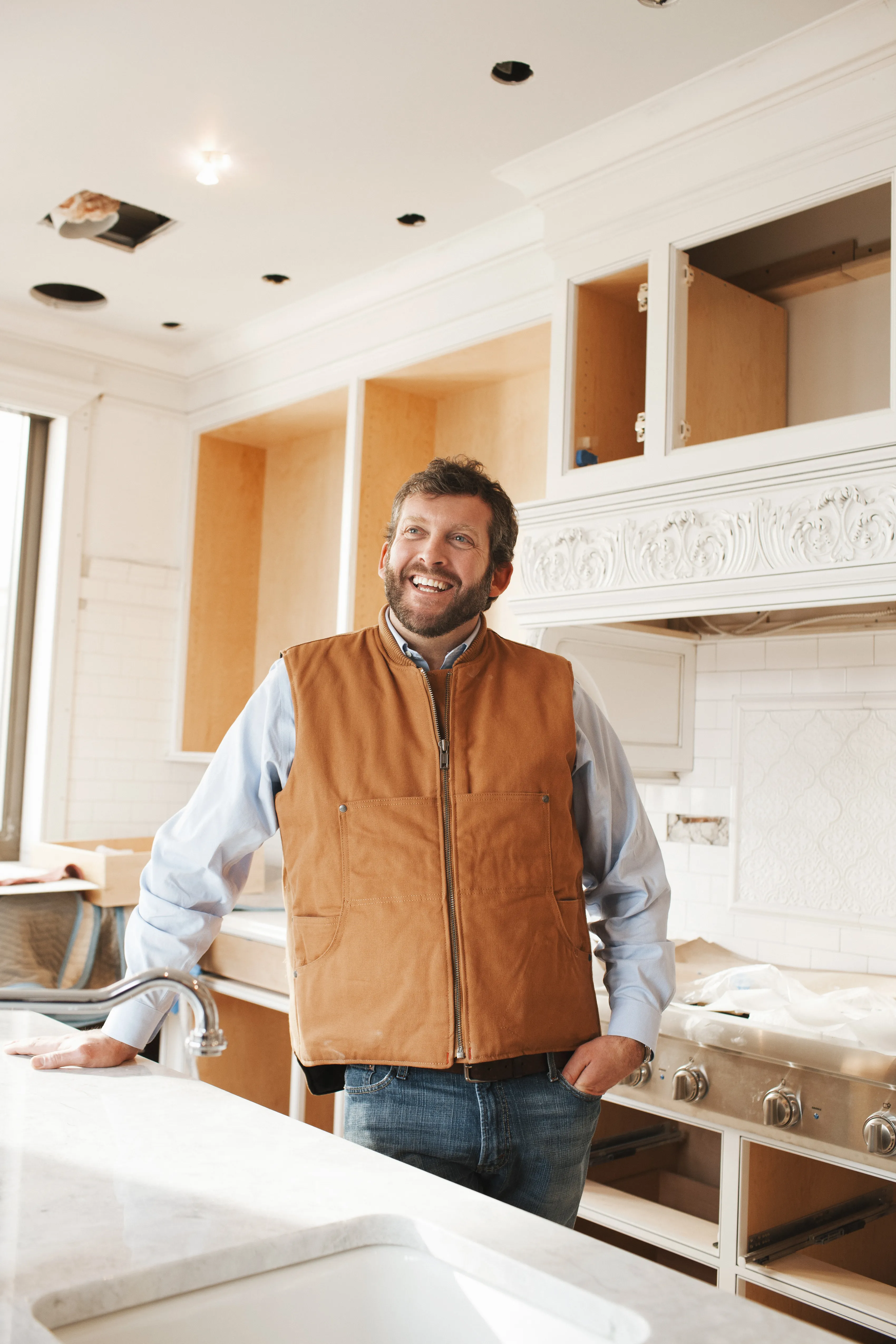 Smiling male builder wearing a construction vest, is inside a kitchen under construction. 