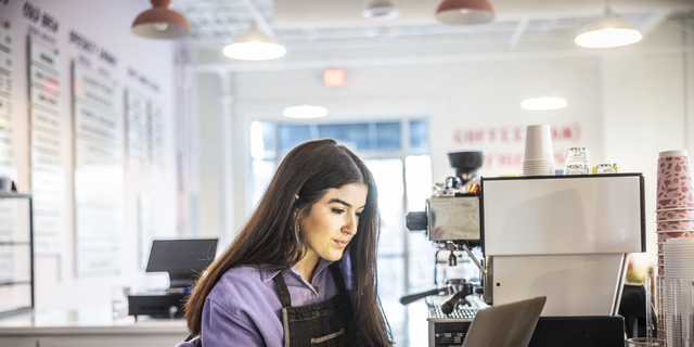 Female coffeeshop owner using laptop in modern coffeeshop