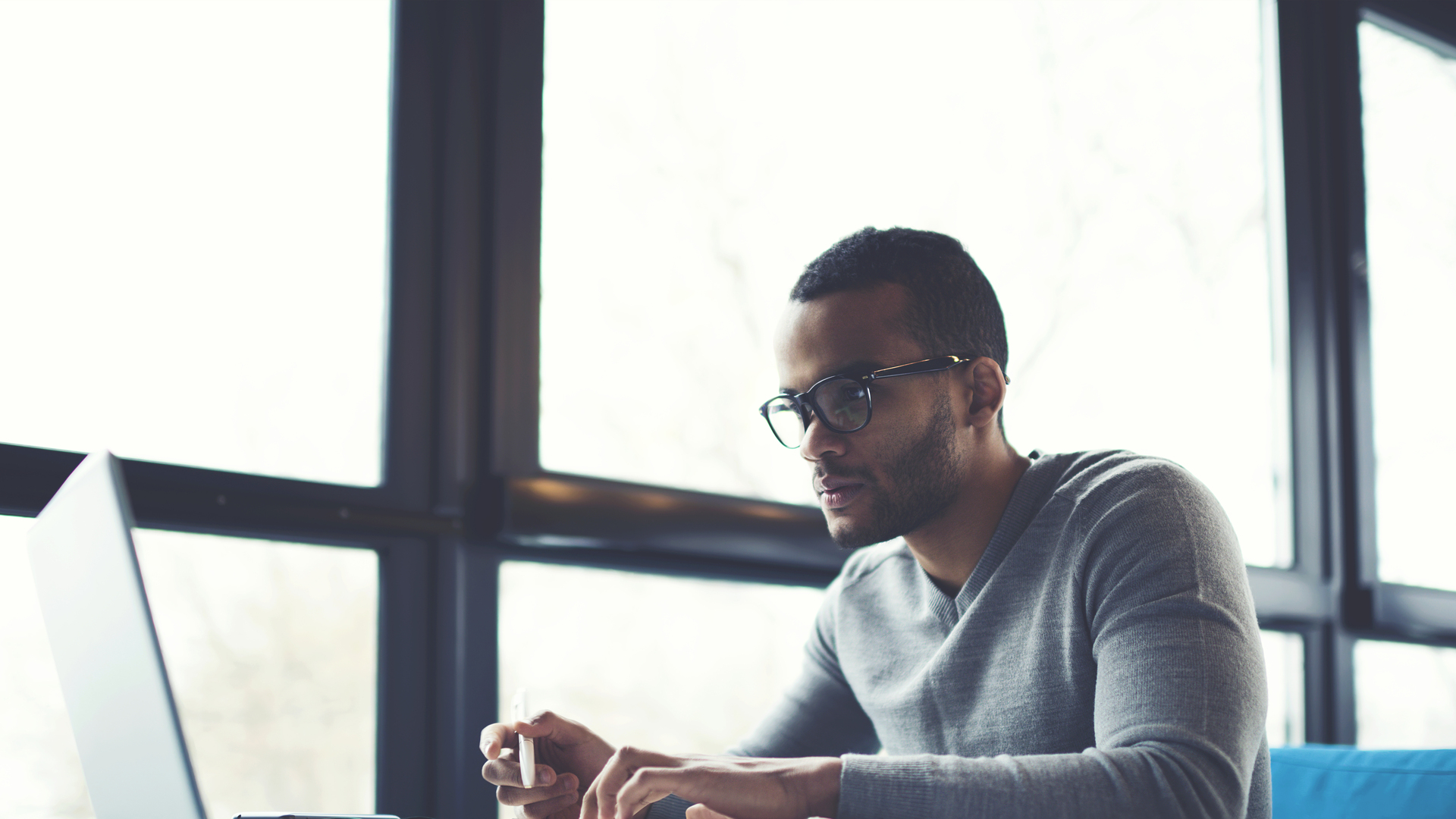 Concentrated businessman checking accounting documentation in online database on modern computer connecting to wireless internet connection. Male aro american entrepreneur working on laptop indoors