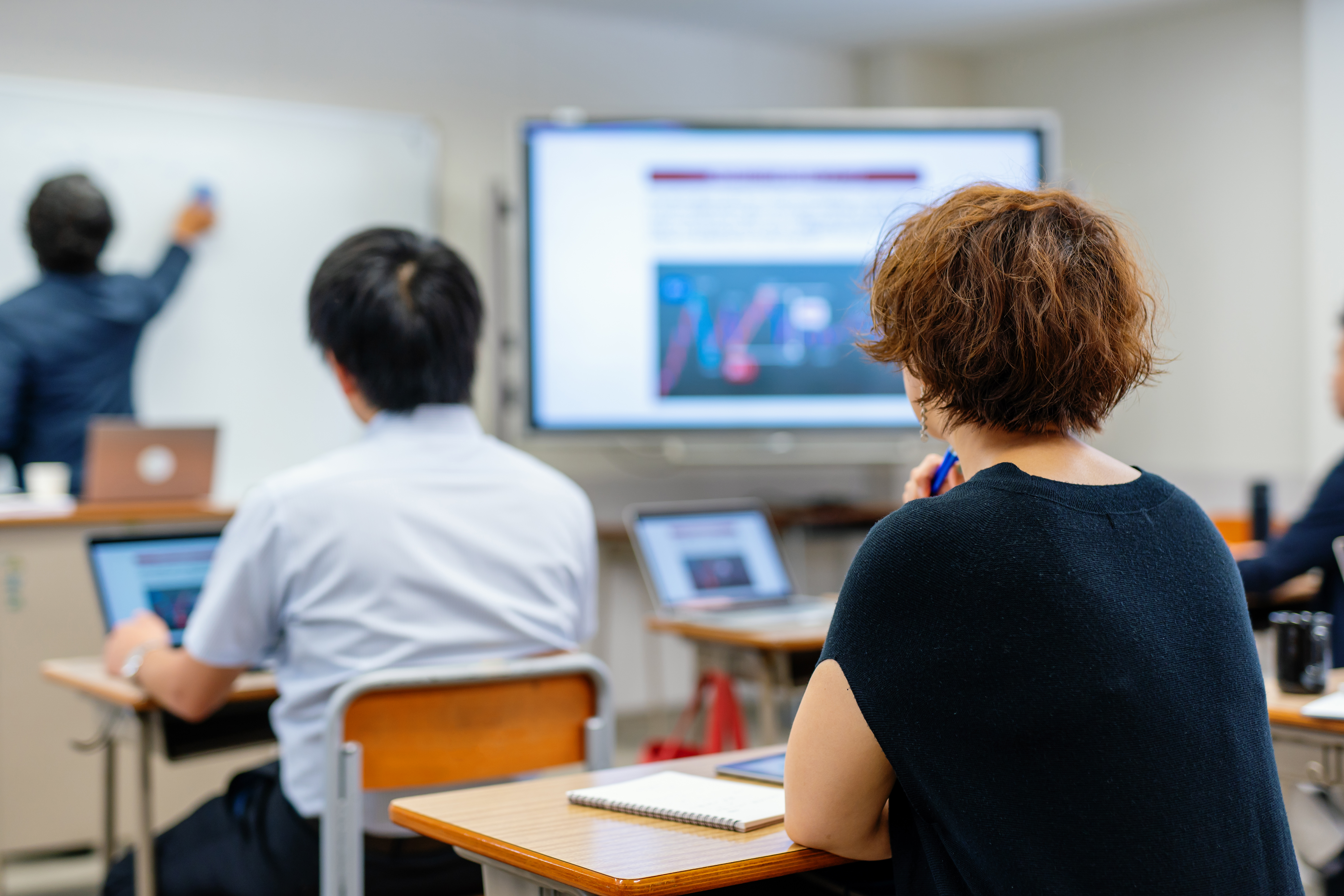 A teacher uses educational technology to support visual learning for students watching a display screen as the teacher clicks through with a remote.