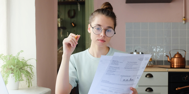 Portrait of young woman, sitting at kitchen table, filling application form, calculating expences, trying to solve budget problems, looking at papers, managing with utility bills