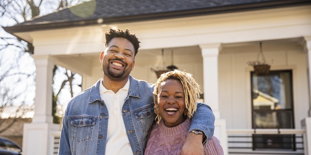 Portrait of husband and wife embracing in front of home