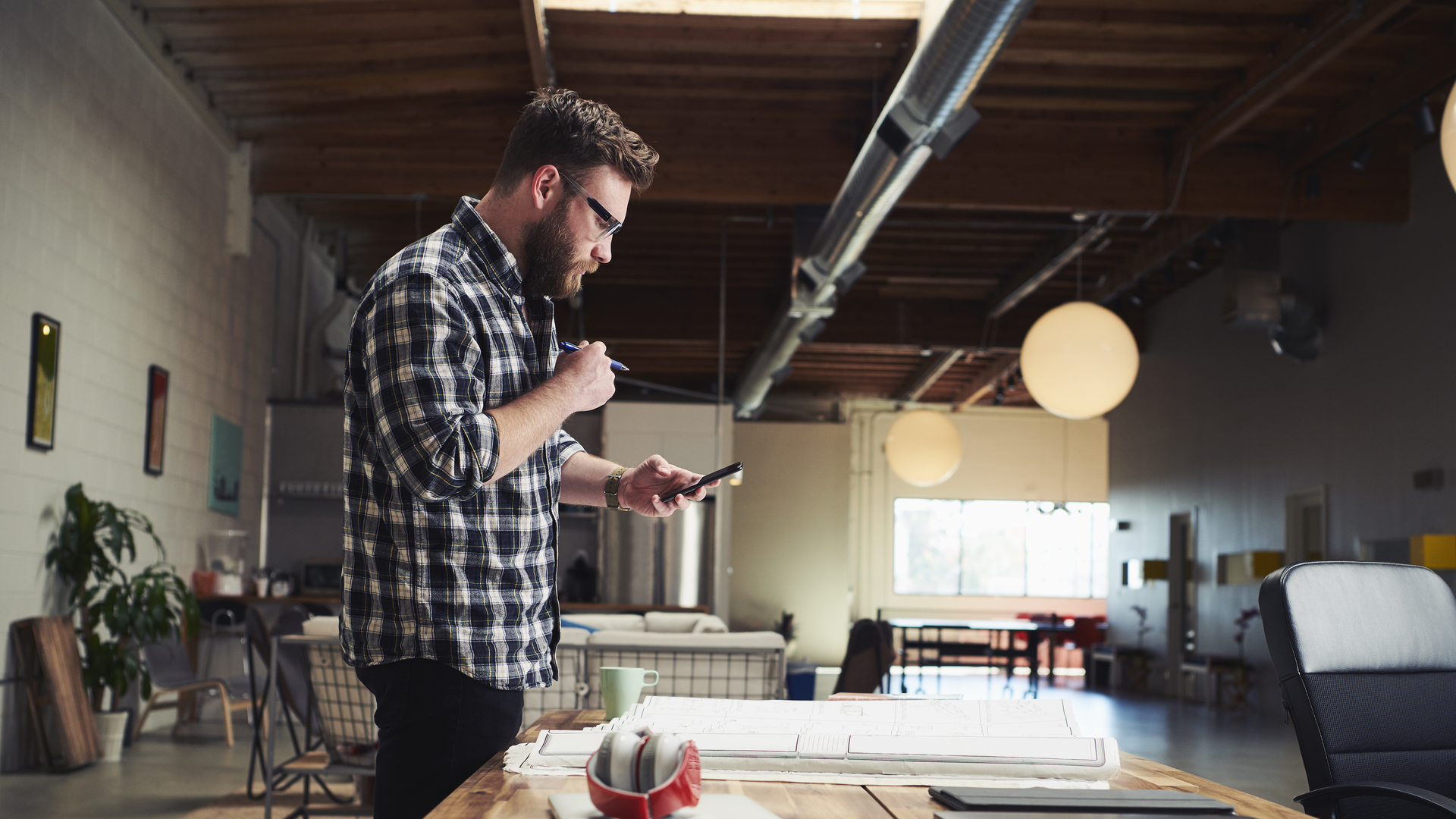 Architect standing at desk looking at mobile phone