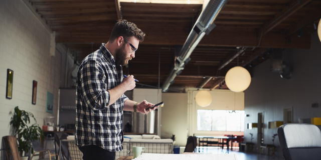 Architect standing at desk looking at mobile phone