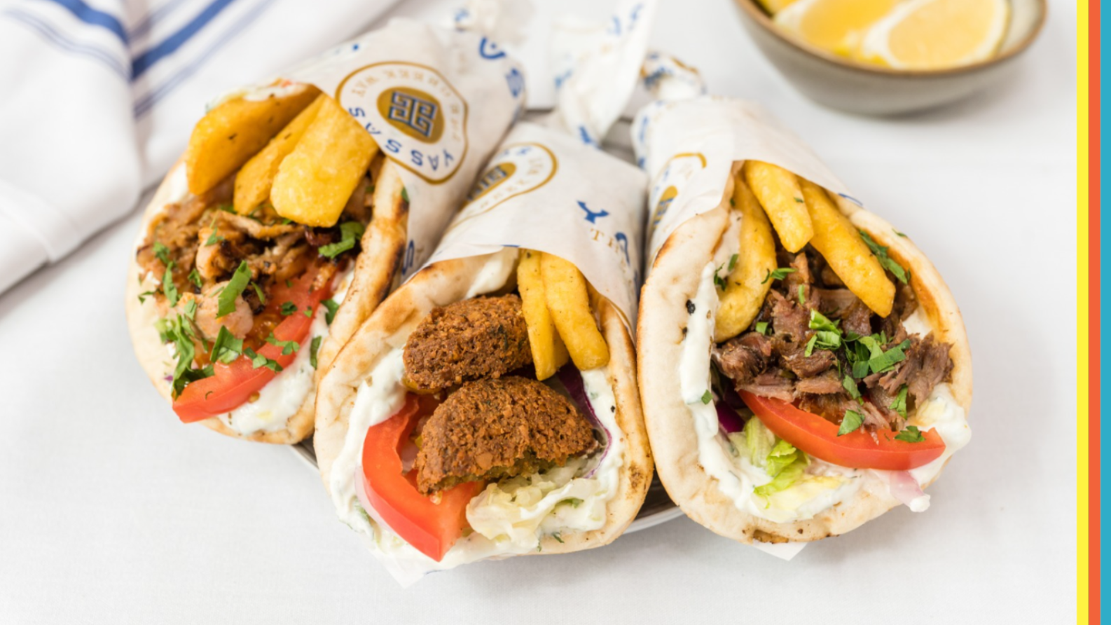 Three freshly made Greek souvlakis filled with meat, falafel, salad, chips and tzatziki, wrapped in pita bread and served on a plate.