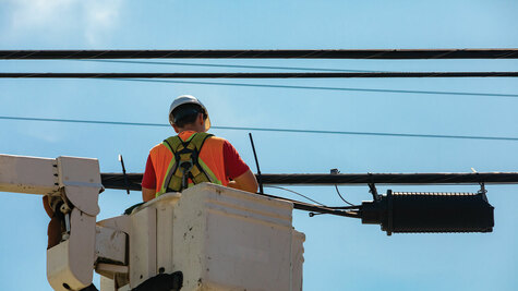 Field technician in a bucket truck working on aerial fiber optic cables and a splice enclosure