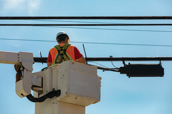 Field technician in a bucket truck working on aerial fiber optic cables and a splice enclosure