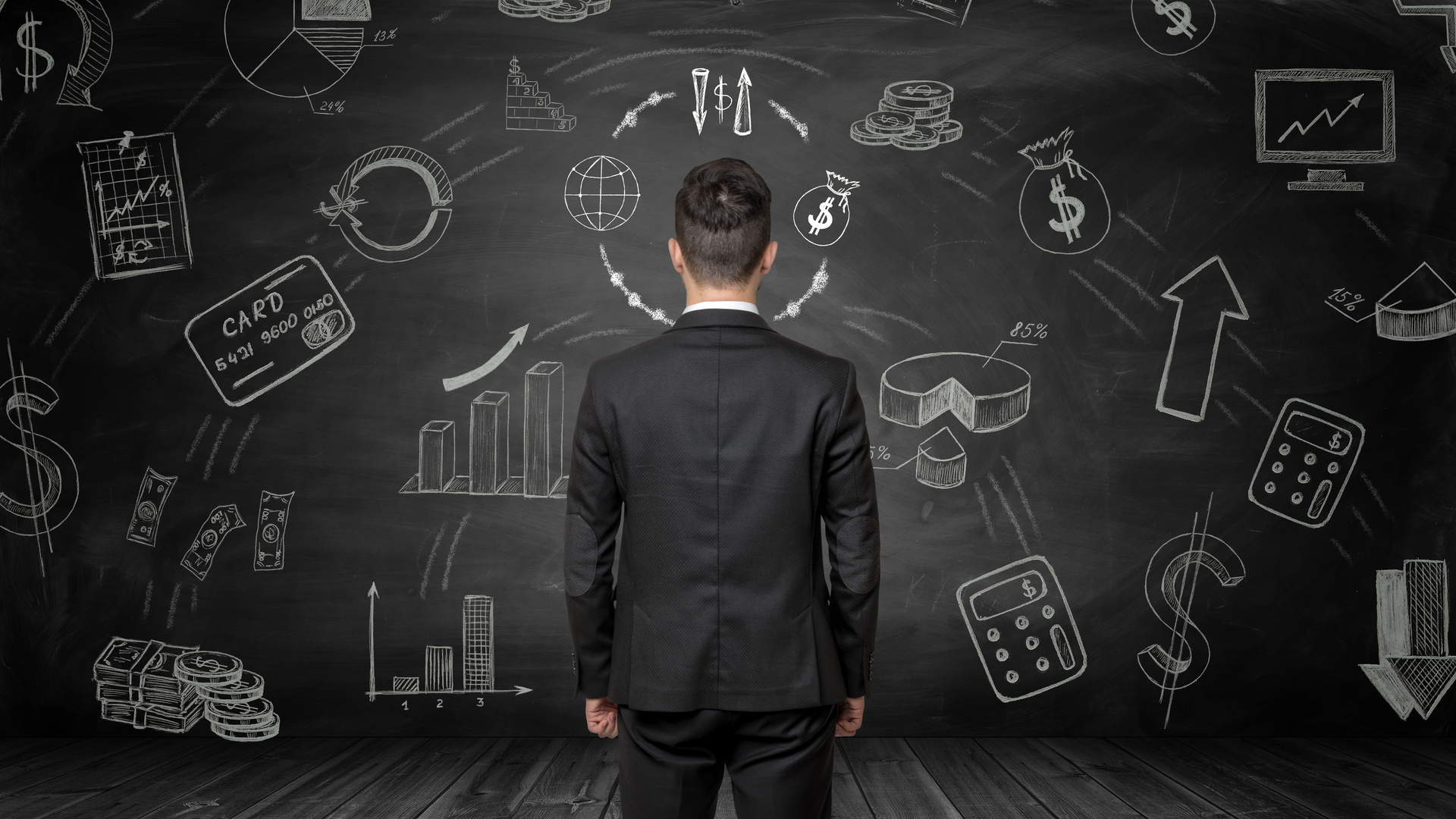 Businessman standing back to us looking at the blackboard with