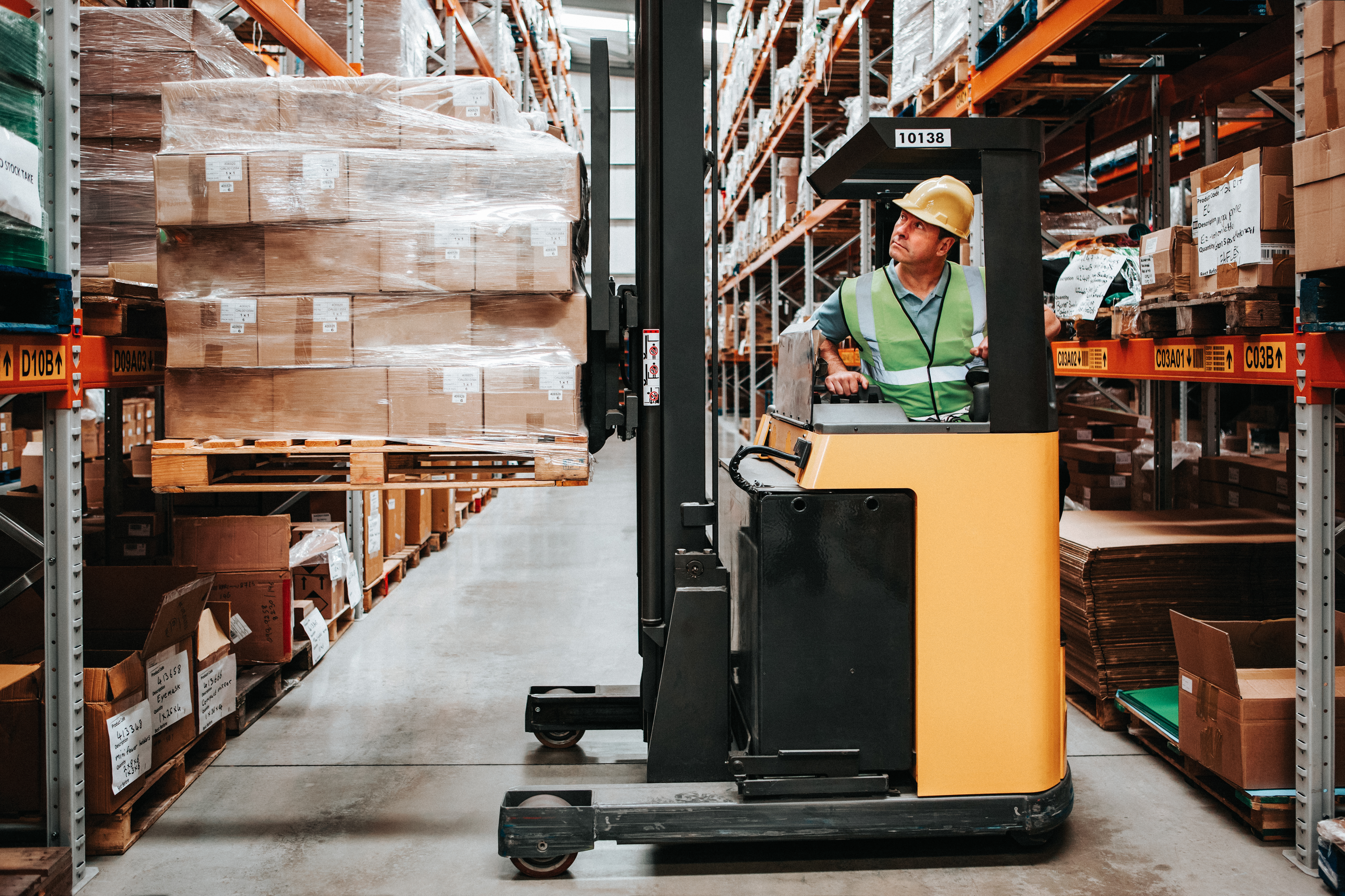Worker operating forklift in warehouse carefully lifting boxes 