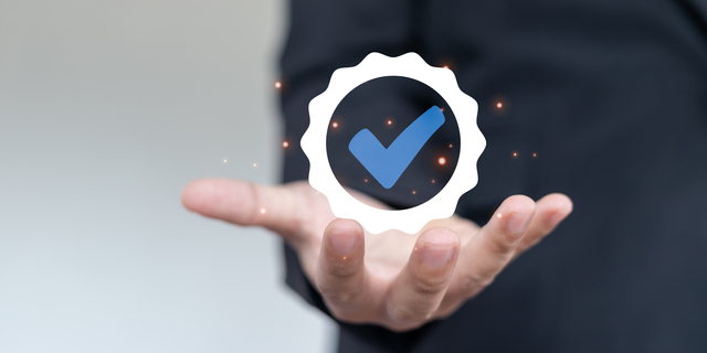 Businessman showing verified check mark badge icon for quality assurance, certification, approval, and business guarantee concept on virtual screen.