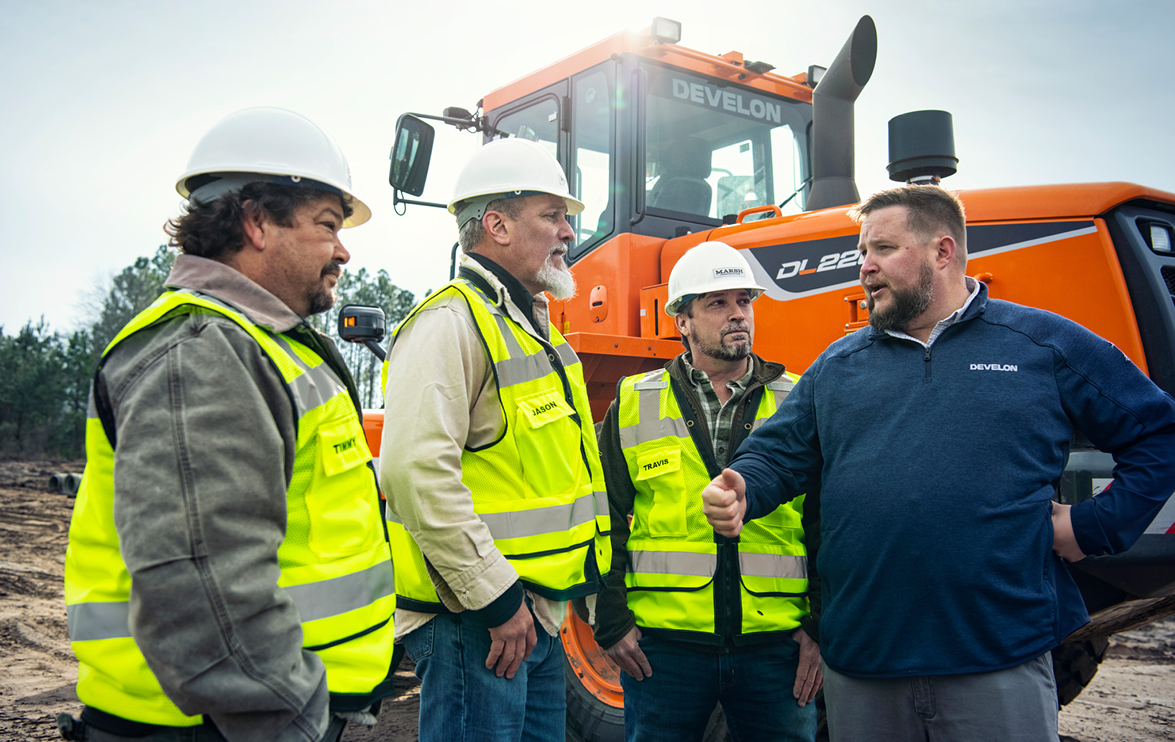 A DEVELON dealer talks with a 3-person crew near a parked DEVELON DL220-7 wheel loader.