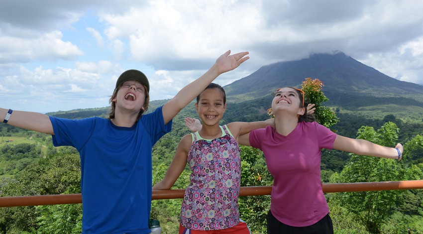 Young children smile and wave their arms in front of a volcano in Costa Rica