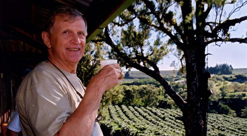 A man smiles at the camera while holding a cup of Costa Rican coffee