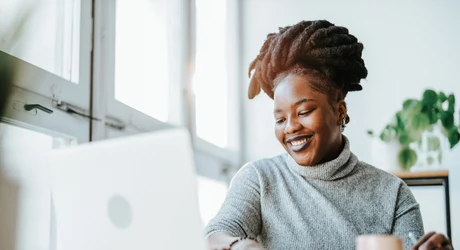 Smiling African American woman working on laptop in brightly lit office 