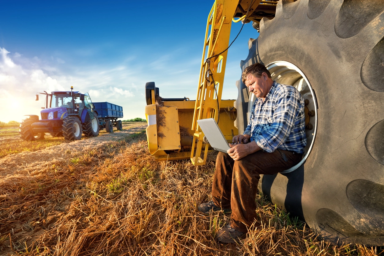 Stock photo of a farmer sitting on a tractor with a laptop.
