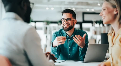 Friendly professional man gesturing with his hands to couple across the desk in office 