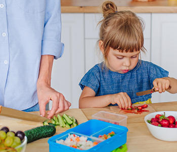 Malčica v kuhinji mami pomaga pripravljati zelenjavo.