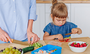 Malčica v kuhinji mami pomaga pripravljati zelenjavo.