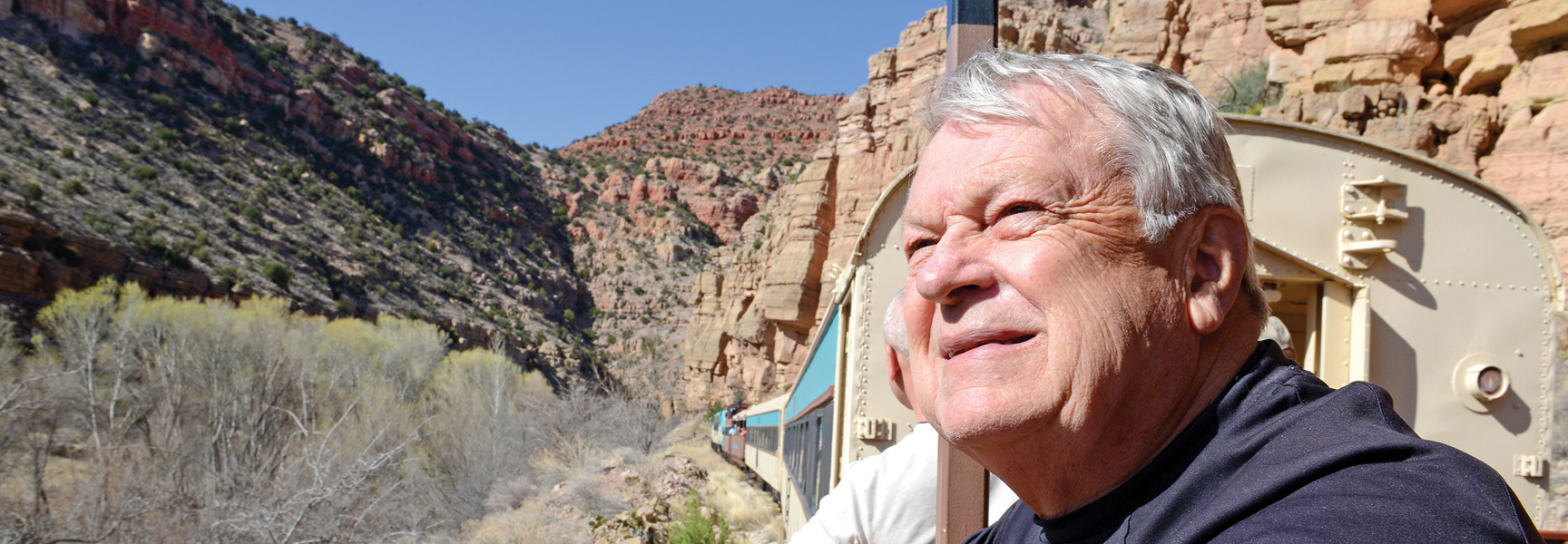 A man enjoys the sunny view of the Arizona canyons from a scenic railroad train.
