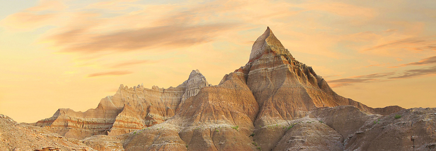 The dramatic, layered rock formations of the Badlands in South Dakota are illuminated by a warm, golden sunset.