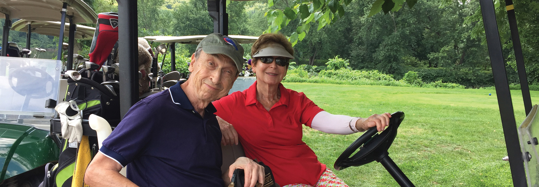 An older couple smiles from their golf cart on a lush green golf course in Pennsylvania on a sunny day.