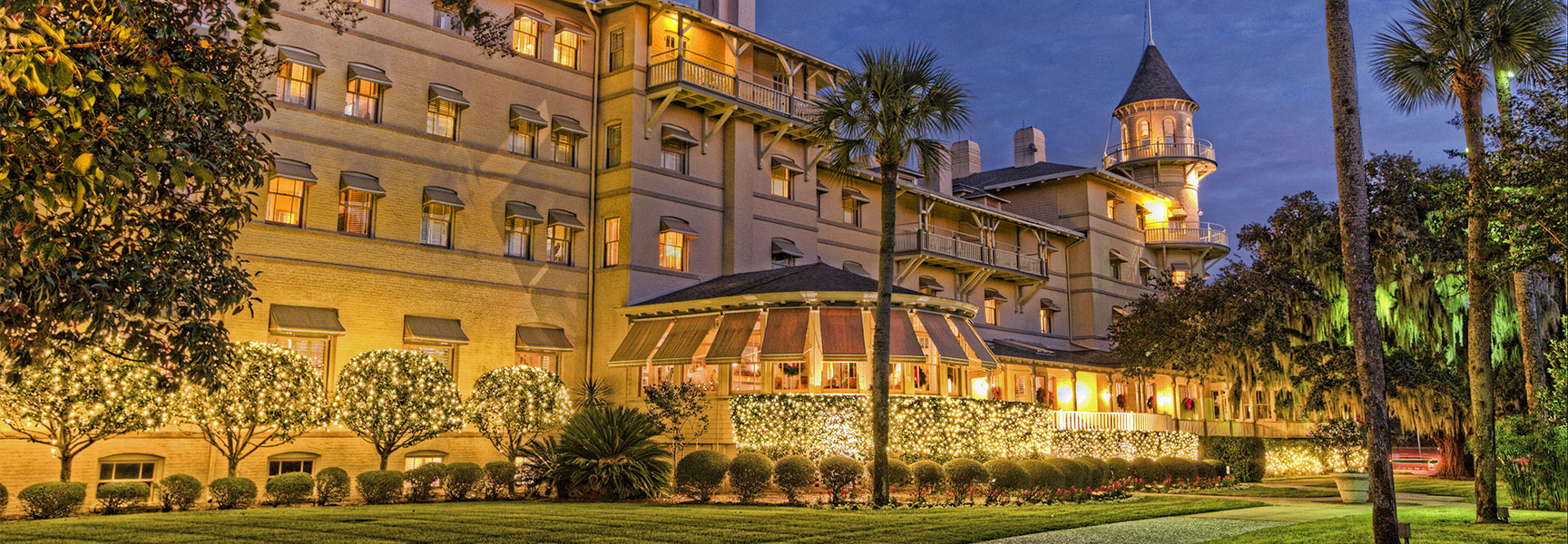 The grand Jekyll Island hotel in Georgia is decorated with glowing Christmas lights on the surrounding trees and grounds at dusk.