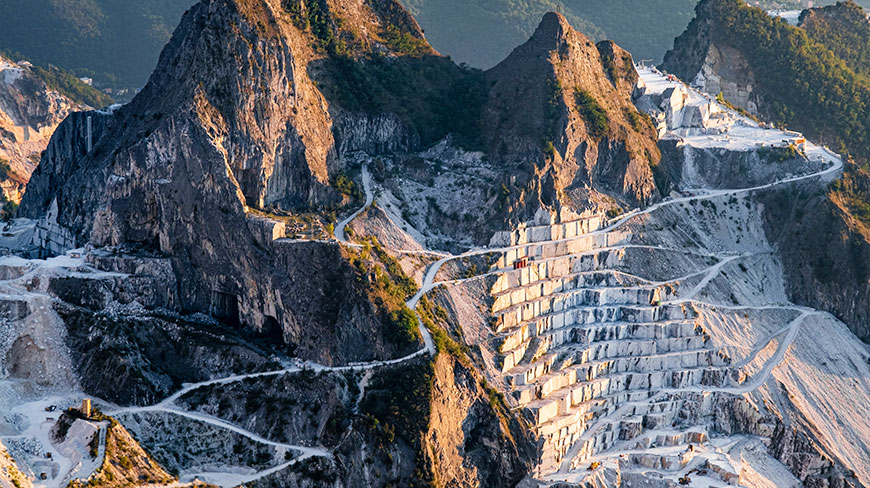 An aerial view of the massive, terraced Carrara marble quarries cut into the rugged mountains of Italy.