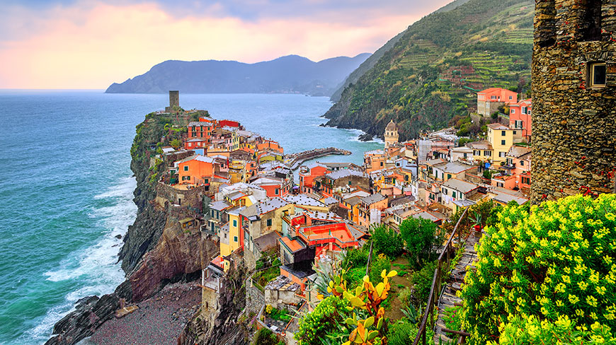 The colorful village of Vernazza in Cinque Terre, Italy, viewed from a cliffside overlooking the Mediterranean Sea at dusk.