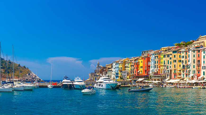 Colorful buildings line the harbor of Portovenere, Italy, where many boats are docked on a sunny day.