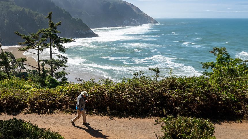 A person walks along a coastal trail overlooking the Pacific Ocean in Oregon.