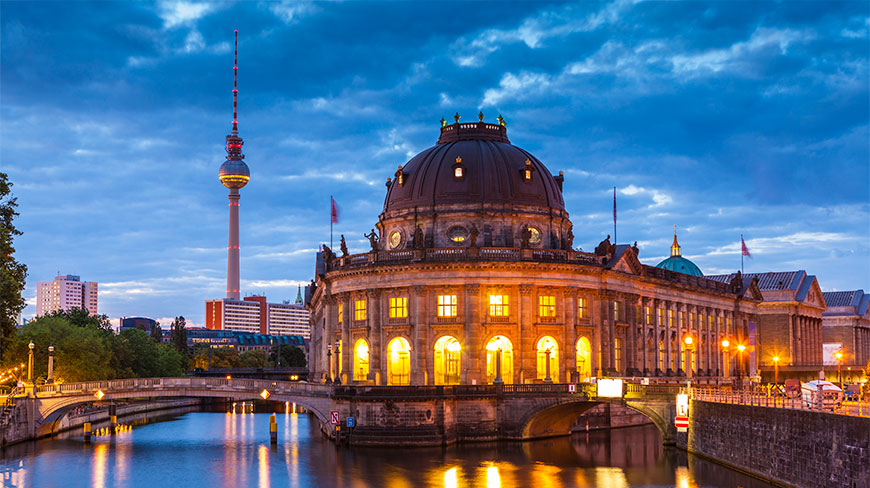 The Bode Museum and TV Tower in Berlin, Germany, are illuminated at dusk with their lights reflecting on the river below.