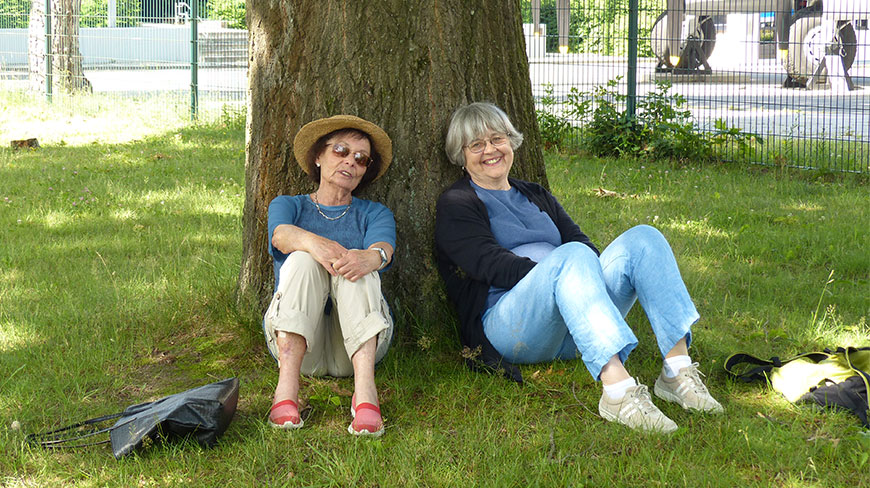 Two women relax in the shade of a tree in a grassy park in Germany.