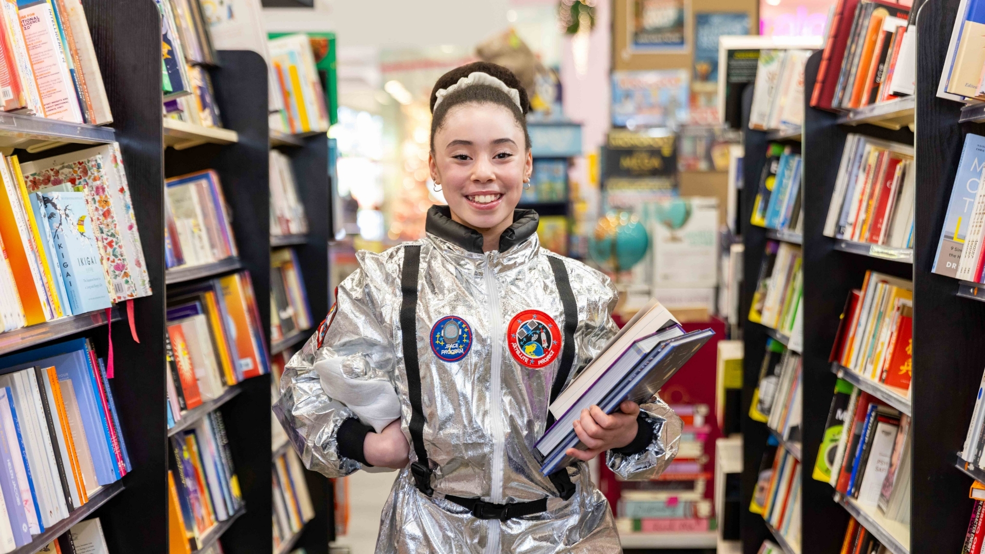 Girl in spacesuit holding books in a QBD aisle