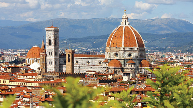 A classic cityscape of Florence, Italy in Tuscany, featuring the iconic red-tiled dome of the Duomo against a backdrop of distant mountains.