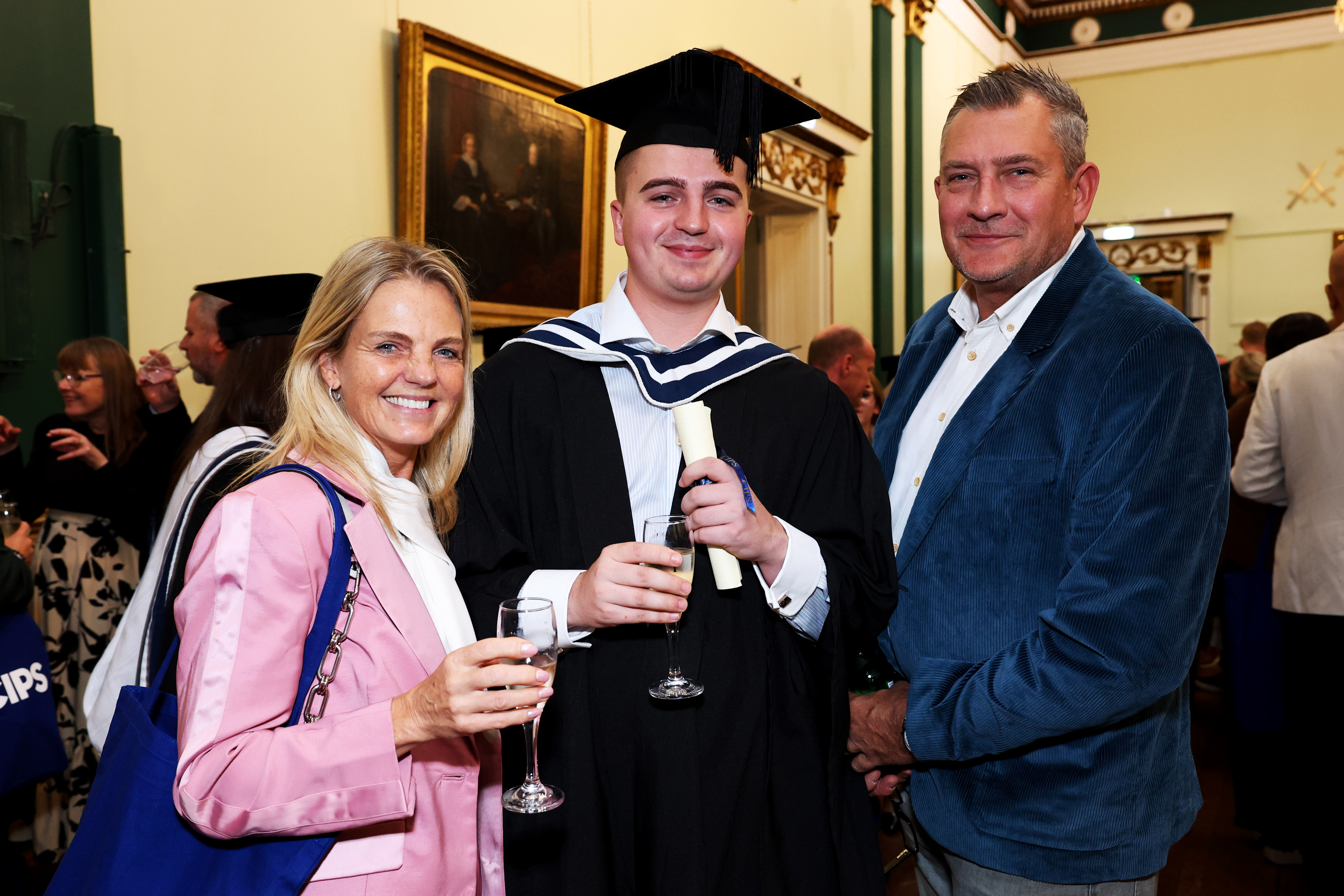 Man in graduation cap and gown celebrating with his parents, holding drinks and posing for a picture