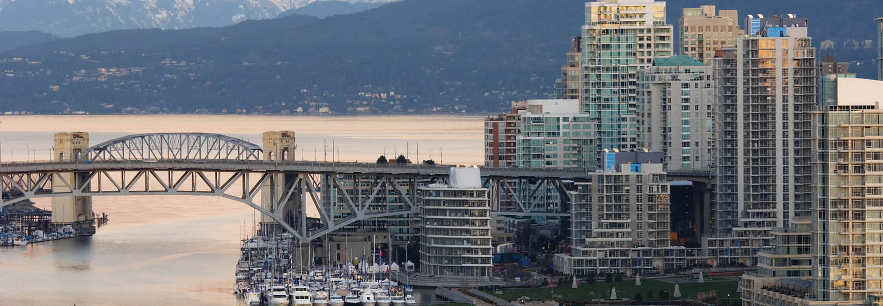 The Burrard Bridge in Vancouver, British Columbia, with the city skyline and mountains in the background at dusk.