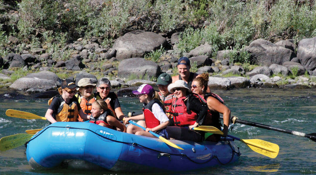 A smiling family in life jackets rafts down the Yellowstone River in Montana during a Yellowstone National Park outdoor adventure trip.