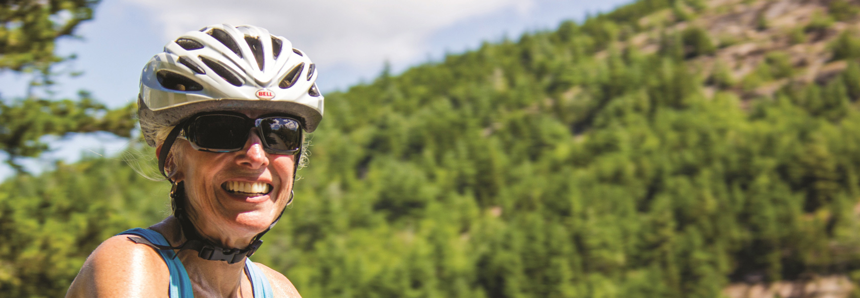 A woman in a helmet and sunglasses smiles while bicycling in Acadia National Park, Maine.