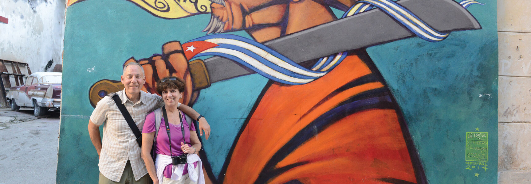 A man and woman pose in front of a colorful street mural in Cuba during a learning adventure.