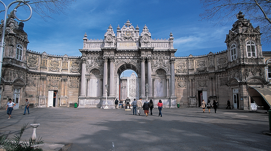 People walk across the courtyard in front of the ornate stone entrance gate of the Dolmabahçe Palace in Istanbul, Turkey.