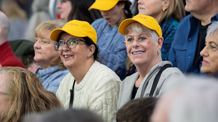 Two smiling women wearing yellow hats sit in the crowd at the Westminster Kennel Club Dog Show at the Javits Center in New York.