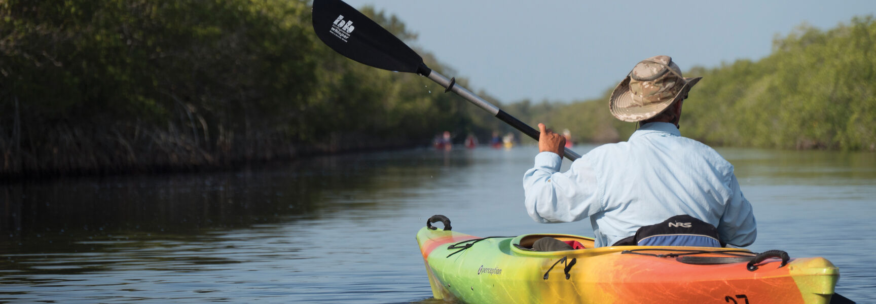 A person paddles a colorful kayak through calm Florida waterways lined with lush green mangroves.